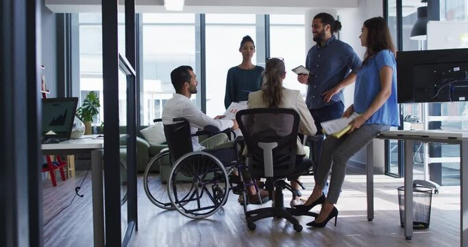 Diverse group of work colleagues talking at casual office meeting, one in wheelchair