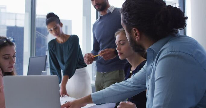 Diverse group of male and female creative colleagues gathered at a table with laptop in discussion