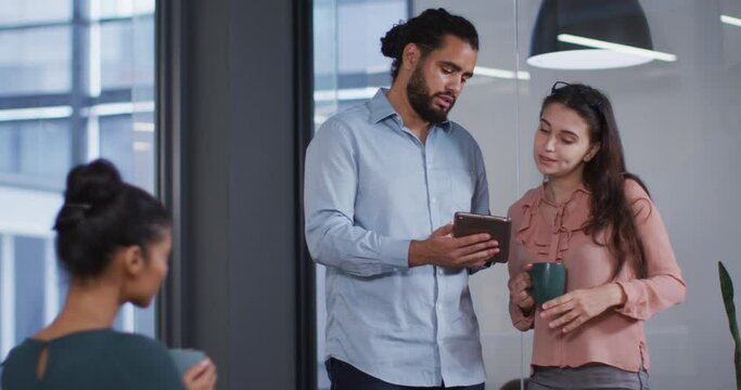 Diverse smiling male and female business colleagues looking at tablet and talking at work