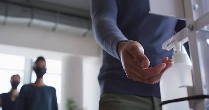 Work colleagues wearing face masks using sanitizer to disinfect hands as they enter the workplace