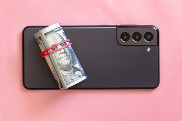 Phantom Grey smart phone and roll of 100 dollar banknotes