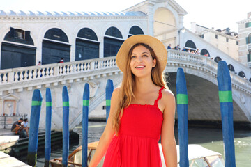 Beautiful young woman with a red dress is standing in front of the famous Rialto Bridge in Venice, Italy © zigres