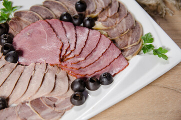 thin slices of beef tongue and beef with olives on white plate