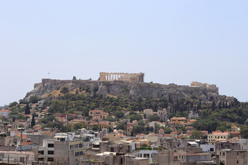 Obraz premium The ancient Acropolis of Athens, Greece and neighborhood below are shown from an elevated view, during daytime in the 2010s. There is room in the blue sky above to add text / copy.