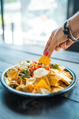 Nachos con cheddar, crema, guacamole, aguacate y pico de gallo con mano