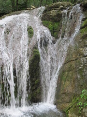Waterfall on a mountain river, water jets against the background of rocks and green moss, Crimea
