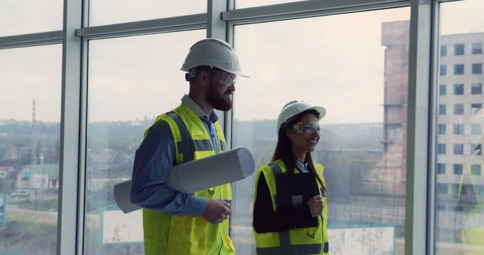 Follow up shot of smiling woman architect and chief male engineer walking through construction site of new commercial center, having pleasant conversation, looking proud and satisfied.