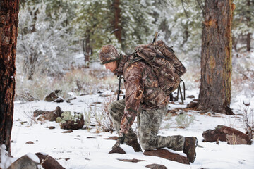 gun hunter kneeling in snowy scene kneeling to inspect deer tracks