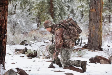 Fotobehang gun hunter kneeling in snowy scene kneeling to inspect deer tracks © Nathan Allred