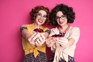 Two cute girl friends woman looking like nerd accountants standing on a pink background. They wear...