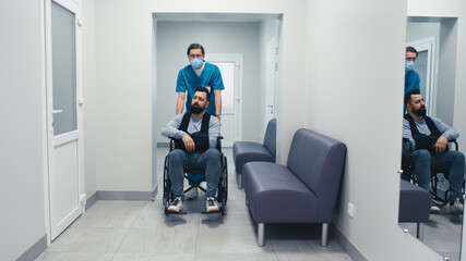 Naklejka na ściany i meble Handicapped male patient on wheelchair speaking with doctor in corridor