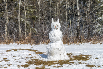 City park snowman made after spring snowfall with a wood background