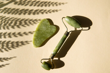 Jade Gua sha scraper and facial massager on beige background.