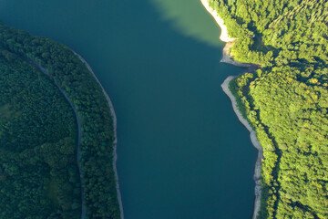 Top down aerial view of big lake with clear blue water between high mountain hills covered with dense evergreen forest.