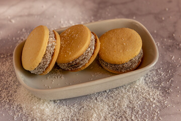 Deliciosos alfajores de maicena rellenos de dulce de leche y espolvoreados con coco rallado, a luz de la mañana.