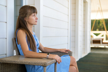 Side view of young beautiful woman resting on fresh air sitting on porch at home. Concept of enjoying nature with good weather.