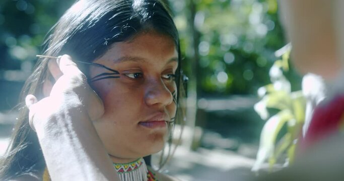 Young Brazilian girl indigenous Patax&oacute; ethnicity doing face painting. 4K.