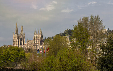 BURGOS, SPAIN - April 9, 2021: Panoramic view of the cathedral of Burgos with several trees and the four flags in front of the European Community Castilla y Leon Spain and Burgos