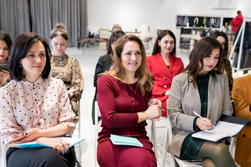 Group of females sitting in the audience for business training. Women outlining coach speech in notebook. People attending personal development seminar or conference. Lifelong learning concept