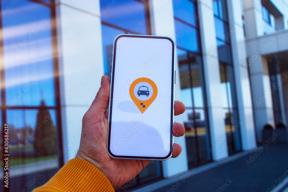 Poster man passenger in the parking lot holds a smartphone with a mobile application and calls a taxi onlin