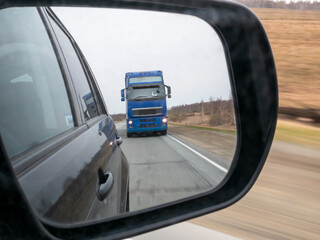 The truck is reflected in the side mirror of the car. Overtaking on the highway, road conditions.