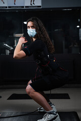 Obraz na płótnie Canvas Girl in EMS suit and medical mask in gym. Protection from coronavirus covid-19. Sport training in electrical muscle stimulation suit at quarantine period.