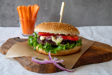 Delicious grilled homemade burger with beef, tomato, onion, cucumber and lettuce and carrot sticks in the background, with copy space