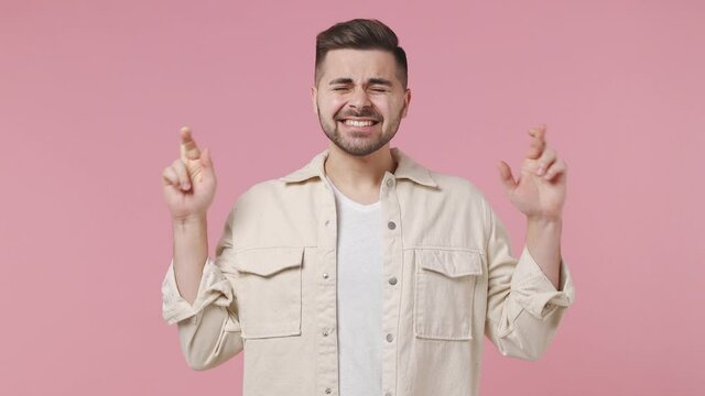 Pleading young man 20s wears light jacket white t-shirt hold hands folded in prayer begging about something make wish keep fingers crossed isolated on pastel pink wall color background studio portrait