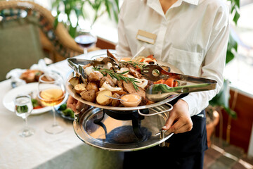 a girl a waiter in a restaurant holds a big hot whore from meat, potatoes and grilled vegetables in her hands