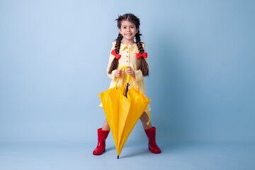 Happy cute little Girl Indian in red rubber boots, cotton dress holds in her hands yellow umbrella zones on a blue background in the studio. concept Spring, space for text