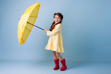 Happy cute little Girl Indian in red rubber boots, cotton dress holds in her hands yellow umbrella...