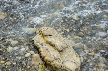pebble stones on the sea beach, the rolling waves of the sea with foam