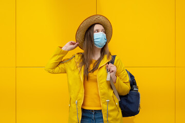 Young modern tourist woman in yellow with face medical mask at the airport station. Travel during...