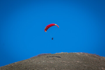 Fototapeta na wymiar Paraglider With Red Parachute Wing Flying in a Blue Sky With Clouds