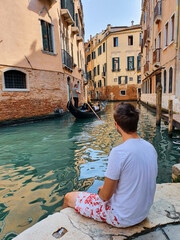 Fototapeta na wymiar Young man looking at a gondola passing by in Venice, Italy.