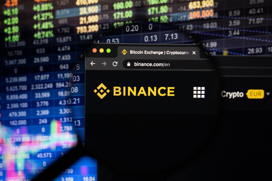 Binance company logo on a website with blurry stock market developments in the background, seen on a computer screen through a magnifying glass