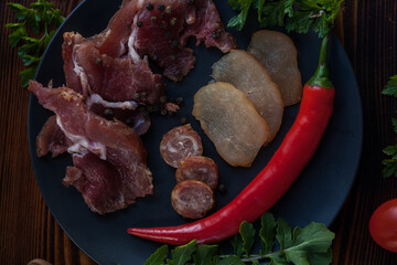 Pieces of meat, pork and chicken, with herbs and paprika. Traditional Ukrainian snacks, cutting board, cold smoked meat cutting on a black plate. View from above. 
