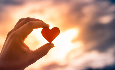 Hand holding heart against beautiful sunset sky setting.
	