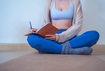 Close up of a Young, unrecognizable woman, pilates instructor, sitting on mat, writing notes to organize the online training session