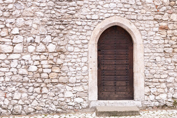 Fototapeta na wymiar Stone wall with door. Old masonry and an old wooden door in the castle wall. Back entrance to one of the castles of Krakow.