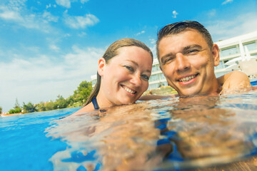 happy young couple resting in swimming pool and smiling at camera