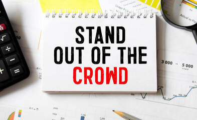 The words Stand out of the crowd written on a white notebook. Closeup of a personal agenda