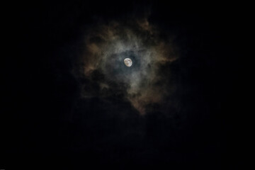 The moon shining through rain filled clouds where the moonlight creates colors as it is reflected...