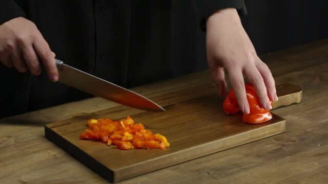 Close-up shot of a girl's hands cutting fresh red bell pepper with a knife on a wooden board. Ingredients for a vegetarian salad. Healthy eating
