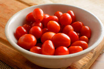 Cherry tomatoes in a white bowl, on a wooden board