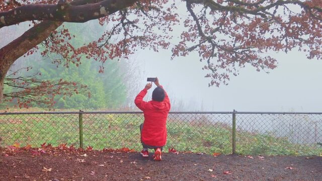 Senior man recording videos of the foggy autumn scene with a smartphone