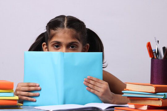little Indian or asian school girl reading book over study table. stack of books