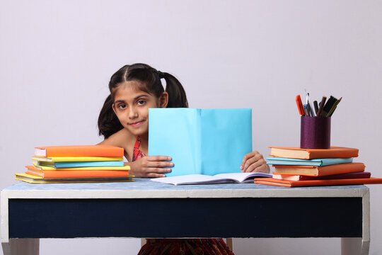 little Indian or asian school girl reading book over study table. stack of books