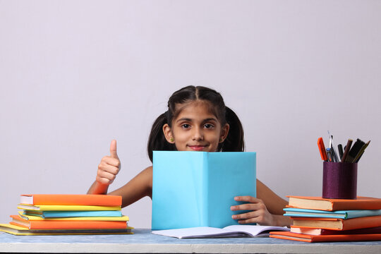 Little Indian Or Asian School Girl Reading Book Over Study Table. Stack Of Books