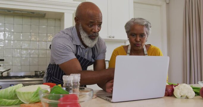 African american senior couple wearing aprons having a video call on laptop in the kitchen at home